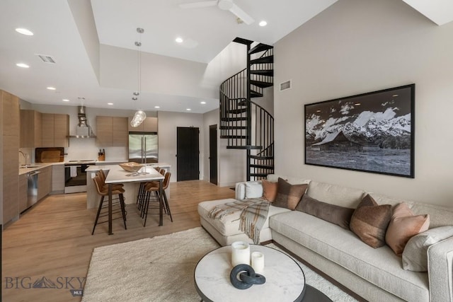 living room featuring ceiling fan, a towering ceiling, sink, and light hardwood / wood-style flooring