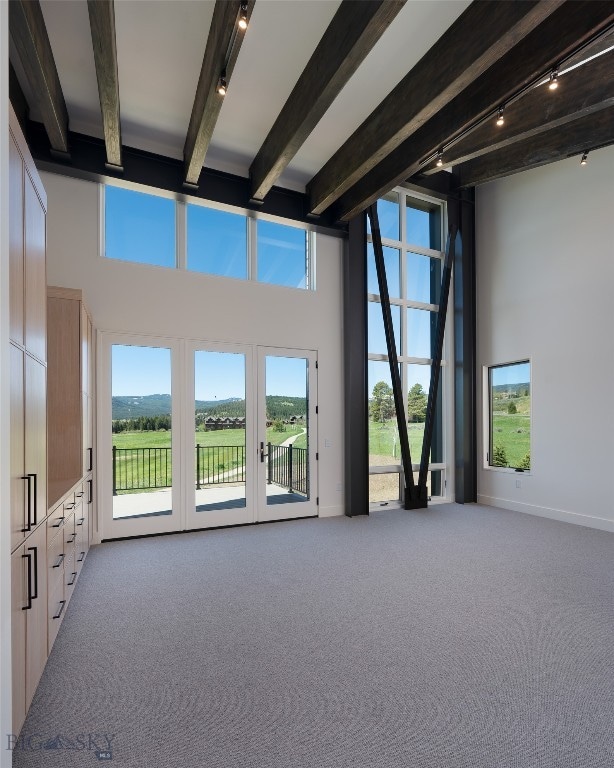 interior space featuring beamed ceiling, a healthy amount of sunlight, a towering ceiling, and light colored carpet