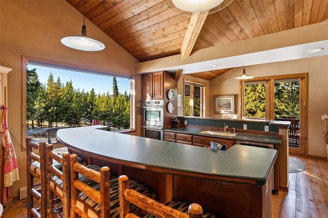 kitchen featuring stainless steel double oven, a peninsula, a sink, vaulted ceiling, and dark countertops