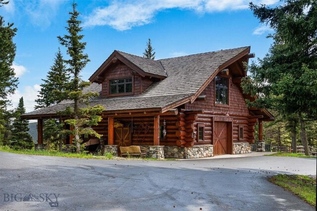 log home featuring driveway, log siding, an outdoor structure, stone siding, and a barn