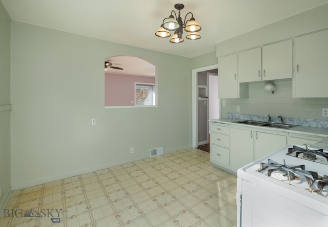 kitchen featuring white cabinets, backsplash, ceiling fan with notable chandelier, and sink