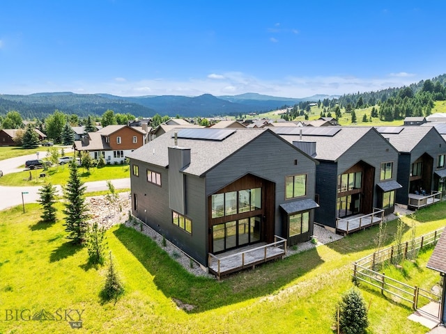 rear view of property with a mountain view, a lawn, and solar panels