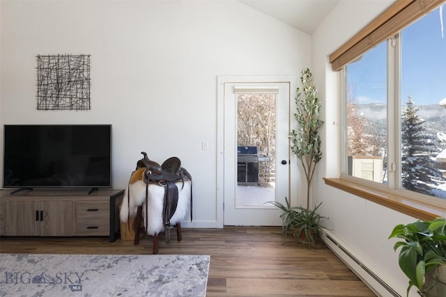 interior space with a healthy amount of sunlight, baseboard heating, vaulted ceiling, and wood finished floors