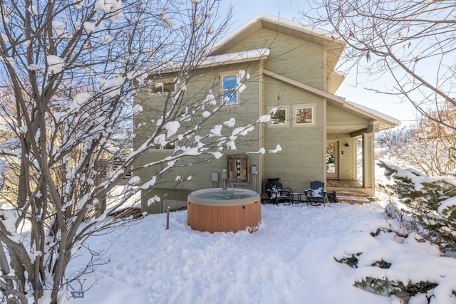 snow covered back of property with central AC unit and a hot tub