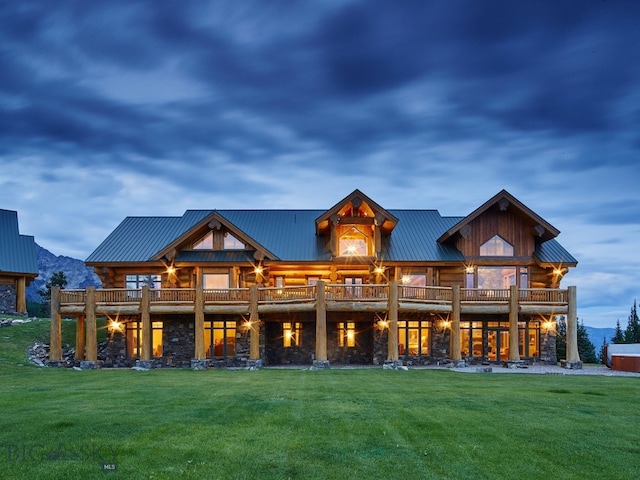 back house at dusk featuring a balcony and a lawn