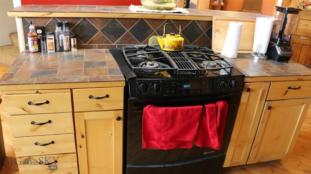 kitchen featuring black gas stove, hardwood / wood-style floors, and tile counters