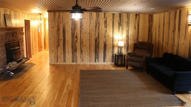 living room with ceiling fan, wooden walls, light hardwood / wood-style flooring, and a fireplace