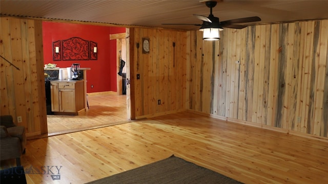 unfurnished living room with wood walls, ceiling fan, and light hardwood / wood-style flooring