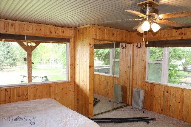 carpeted bedroom with radiator heating unit, wood walls, and ceiling fan