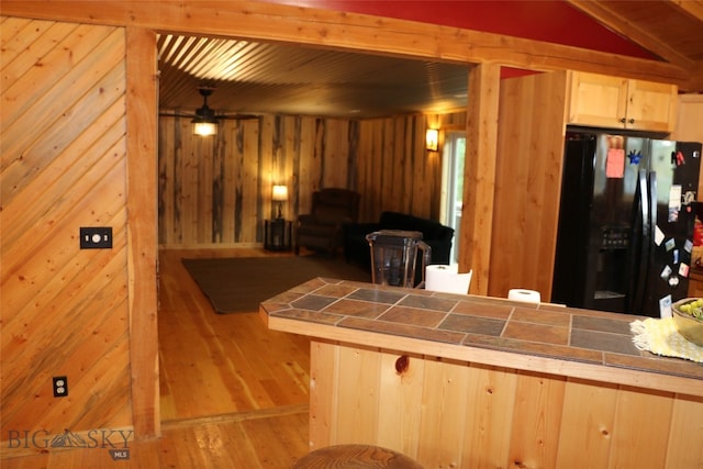 kitchen featuring wood walls, black fridge, and tile countertops