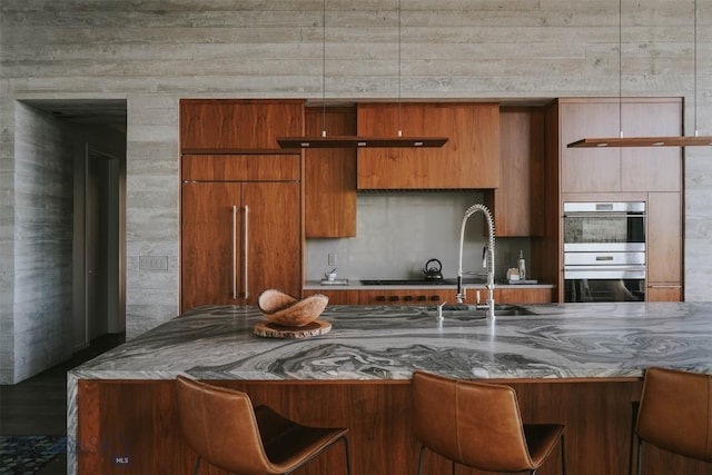 kitchen featuring modern cabinets, brown cabinets, double oven, a kitchen bar, and a sink