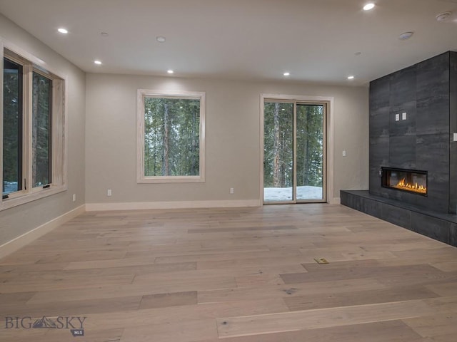 unfurnished living room featuring a healthy amount of sunlight, a tiled fireplace, and light hardwood / wood-style flooring