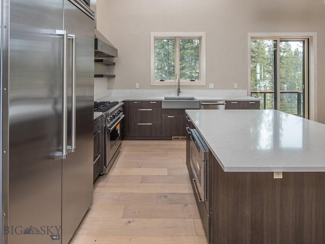 kitchen featuring light wood-type flooring, extractor fan, high end appliances, sink, and a kitchen island