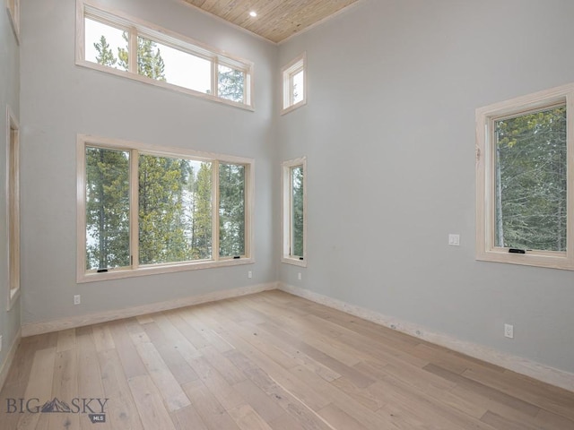 empty room featuring a towering ceiling, wood ceiling, and light hardwood / wood-style flooring