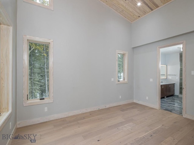 empty room with a healthy amount of sunlight, light wood-type flooring, wood ceiling, and a towering ceiling