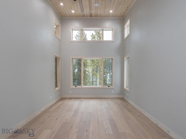 empty room featuring a healthy amount of sunlight, wooden ceiling, a towering ceiling, and light hardwood / wood-style flooring