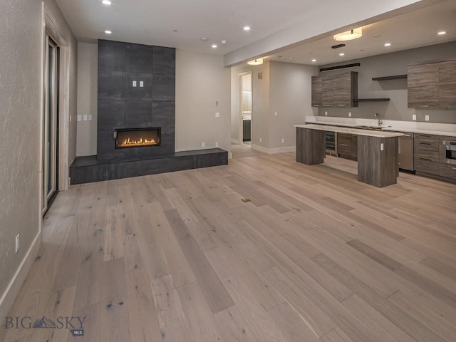 unfurnished living room with a tile fireplace, light hardwood / wood-style flooring, and sink