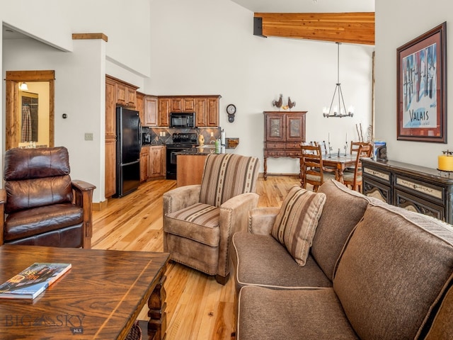 living room featuring a chandelier, light hardwood / wood-style floors, a high ceiling, and beam ceiling