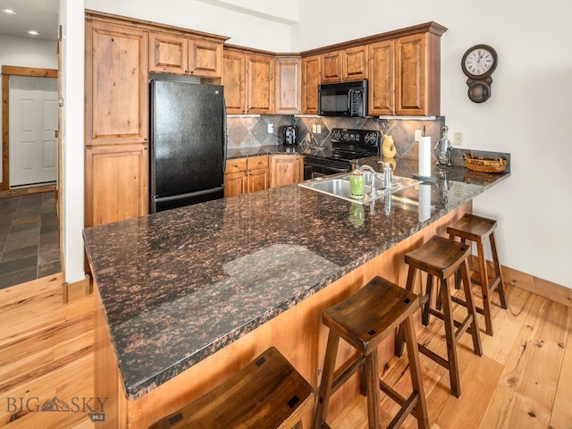 kitchen with a kitchen bar, dark stone countertops, kitchen peninsula, light wood-type flooring, and black appliances