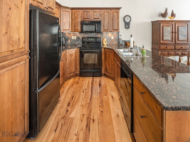 kitchen featuring black appliances, sink, light hardwood / wood-style flooring, dark stone countertops, and tasteful backsplash