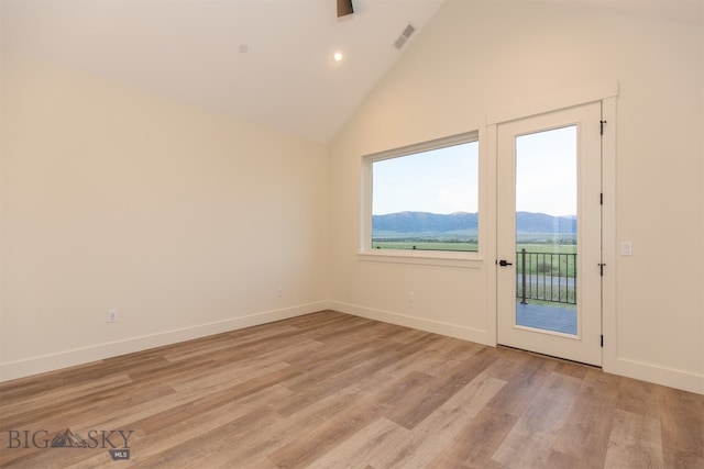 empty room featuring a mountain view, light hardwood / wood-style flooring, and high vaulted ceiling