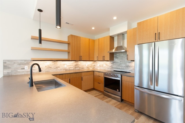 kitchen featuring stainless steel appliances, wall chimney range hood, sink, decorative backsplash, and light wood-type flooring