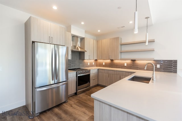 kitchen featuring wall chimney range hood, dark wood-type flooring, appliances with stainless steel finishes, decorative light fixtures, and sink