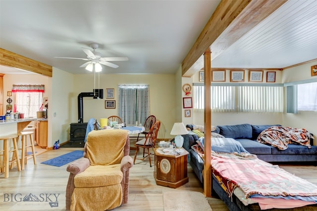 living room with ceiling fan, beamed ceiling, light wood-type flooring, and a wood stove