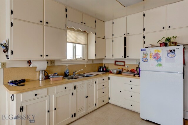 kitchen featuring white refrigerator, sink, white cabinetry, and light tile patterned flooring