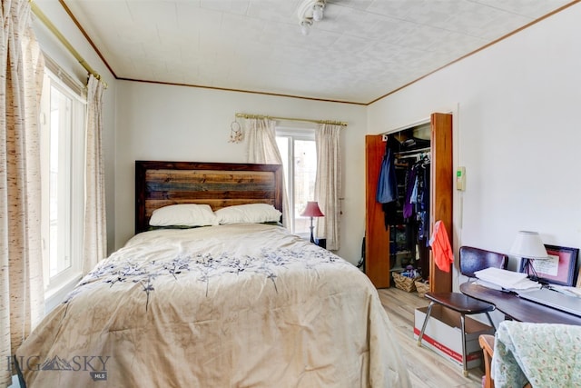 bedroom with light wood-type flooring, ornamental molding, and a closet