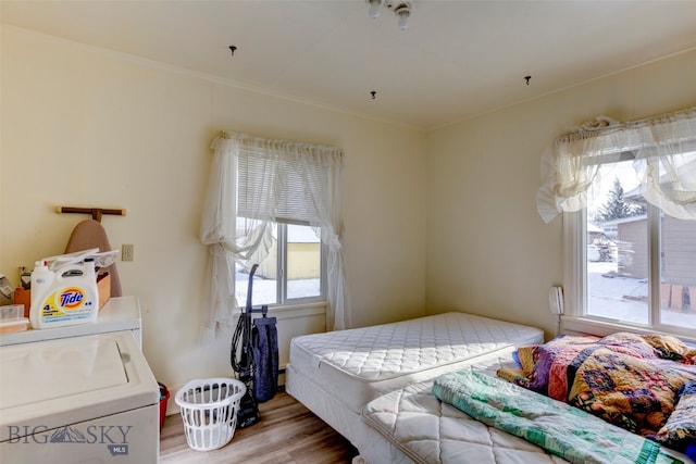 bedroom featuring crown molding, light wood-type flooring, washing machine and clothes dryer, and multiple windows