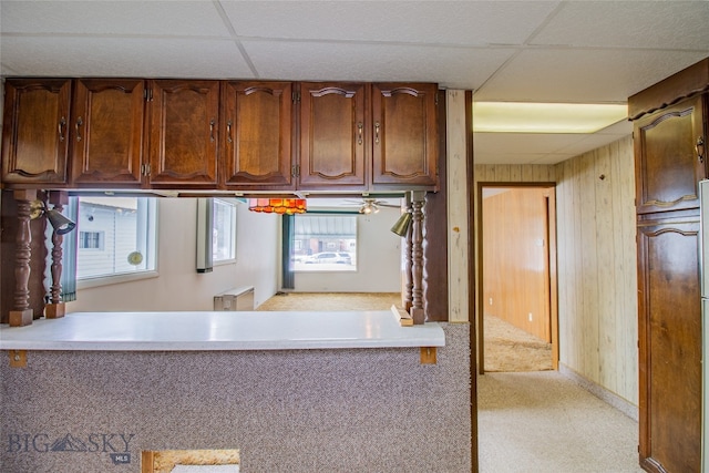 kitchen with light carpet, wood walls, and a drop ceiling