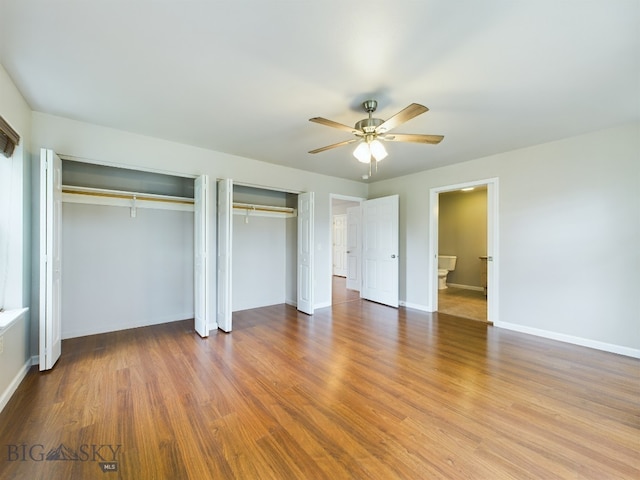 unfurnished bedroom featuring ceiling fan, wood finished floors, two closets, and baseboards