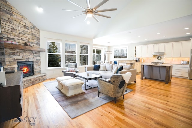 living room featuring a fireplace, light wood-type flooring, ceiling fan, sink, and vaulted ceiling