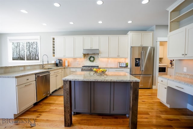 kitchen featuring high quality appliances, a kitchen island, light hardwood / wood-style flooring, white cabinets, and light stone counters