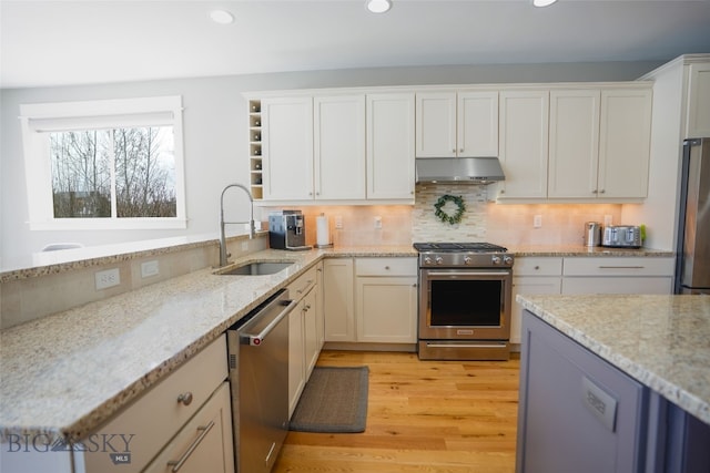 kitchen featuring appliances with stainless steel finishes, white cabinetry, light stone counters, and sink