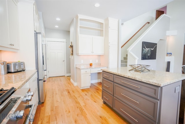 kitchen featuring white cabinets, light wood-type flooring, a center island, light stone countertops, and stainless steel fridge