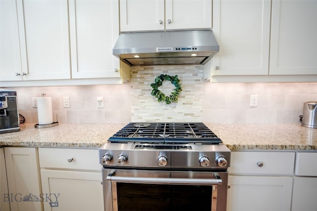 kitchen featuring high end stainless steel range, white cabinets, wall chimney range hood, and tasteful backsplash