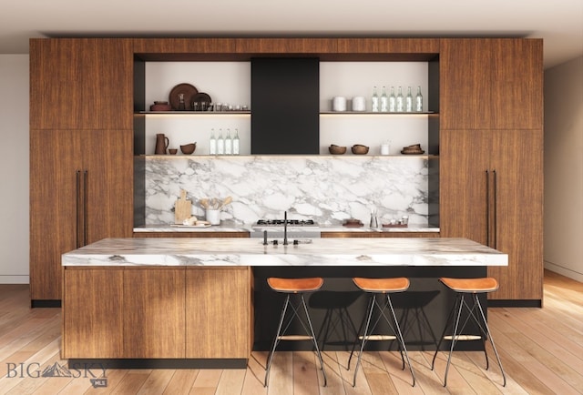 bar featuring stainless steel gas cooktop, light stone counters, and light hardwood / wood-style floors