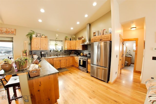 kitchen with wall chimney exhaust hood, stainless steel appliances, tasteful backsplash, kitchen peninsula, and light hardwood / wood-style floors