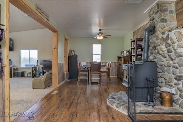 dining space featuring ceiling fan, a healthy amount of sunlight, a wood stove, and dark wood-type flooring