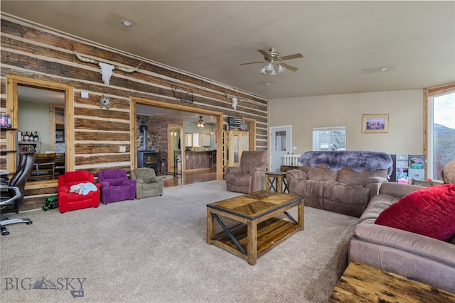 carpeted living room with a wood stove and ceiling fan