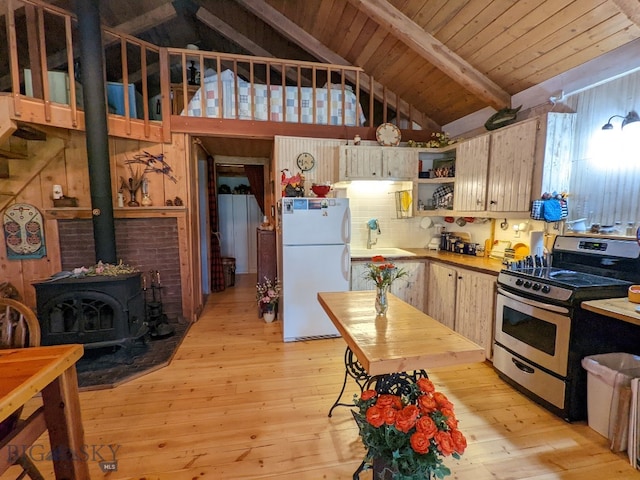 kitchen with stainless steel gas stove, vaulted ceiling with beams, white refrigerator, light wood-type flooring, and a wood stove