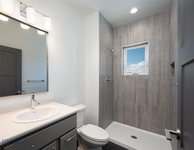 bathroom featuring toilet, a tile shower, and vanity