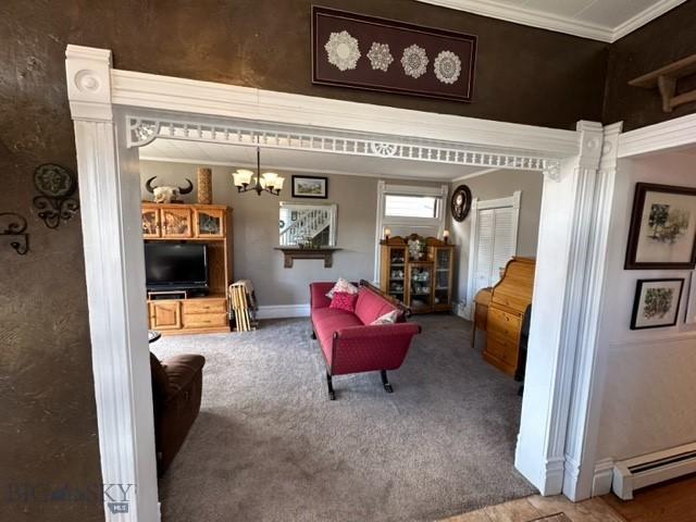 living area with a notable chandelier, a baseboard heating unit, baseboards, carpet, and crown molding