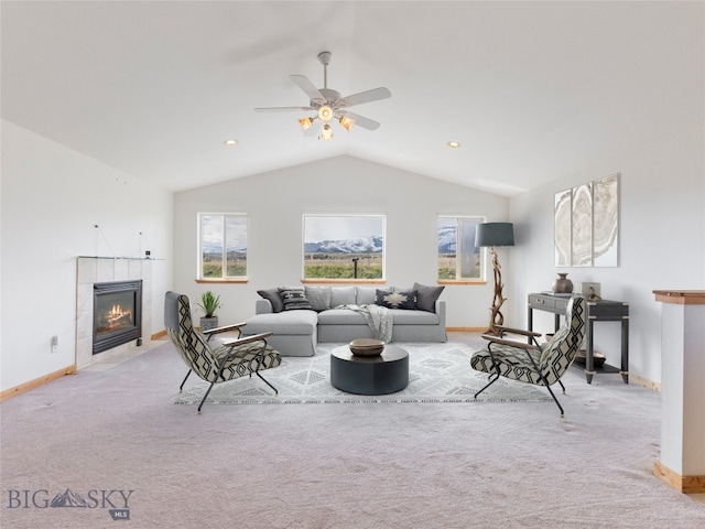 carpeted living room with a tiled fireplace, vaulted ceiling, and ceiling fan