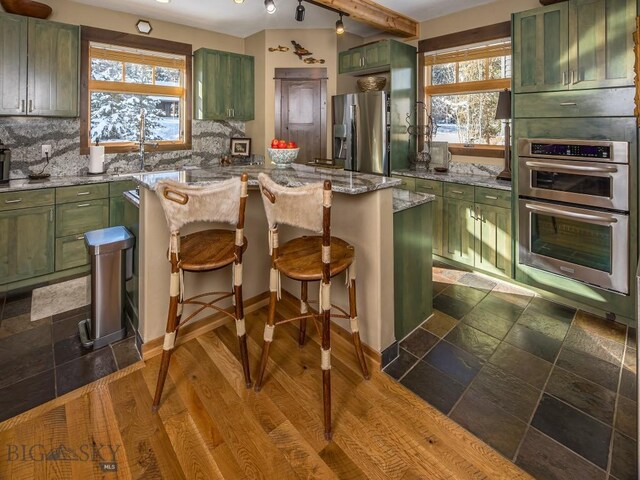 kitchen with backsplash, green cabinetry, dark hardwood / wood-style floors, and stainless steel appliances