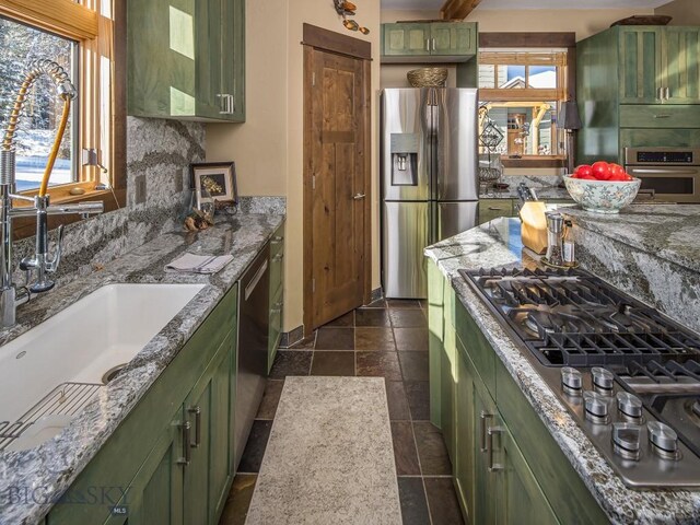 kitchen featuring green cabinets, sink, light stone counters, appliances with stainless steel finishes, and dark tile patterned flooring