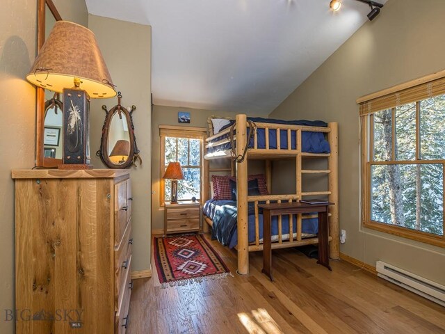 bedroom with baseboard heating, hardwood / wood-style floors, rail lighting, and vaulted ceiling