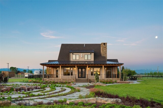 back house at dusk with covered porch and a yard